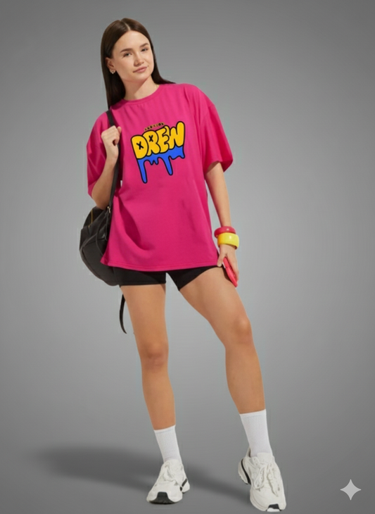 Woman wearing a bright pink oversized t-shirt with colorful text, black shorts, white sneakers, and carrying a black bag on a gray background.