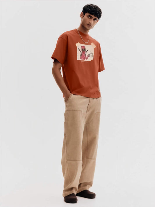 Person wearing a brown t-shirt with dead pool graphic design and beige pants on a white background