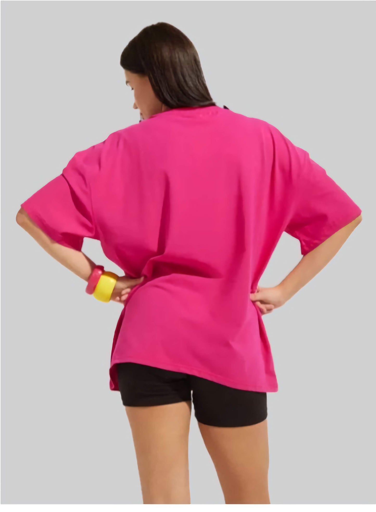 Person wearing a bright pink oversized top and black shorts on a gray background