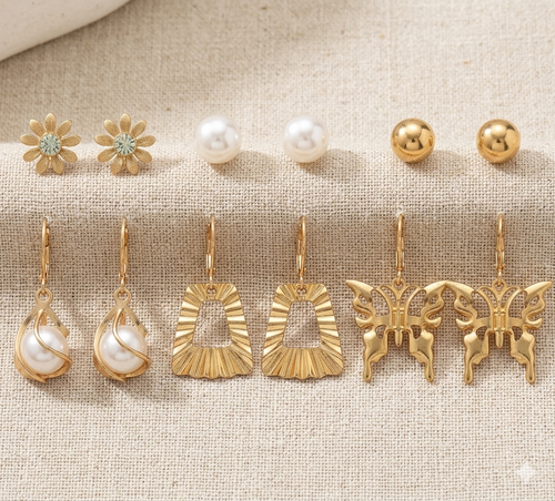 Collection of gold and pearl earrings on a textured beige surface