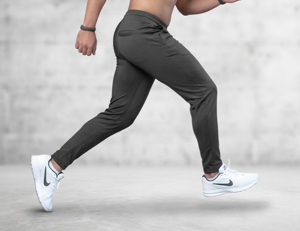 Person wearing dark gray athletic pants and white sneakers on a light gray background
