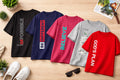 Five t-shirts with motivational phrases on a wooden surface with shoes and sunglasses.