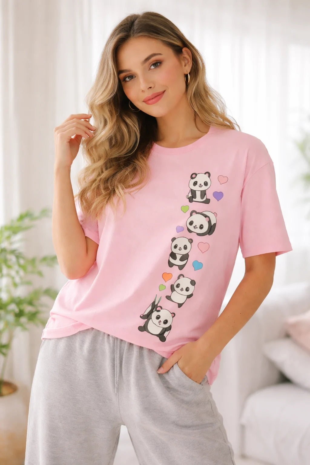 Woman wearing a pink t-shirt with panda designs and gray pants in a bright room.