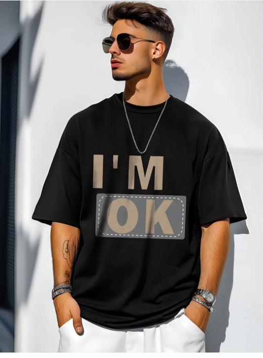 Man wearing a oversized black t-shirt with 'I'm OK' text against a white wall