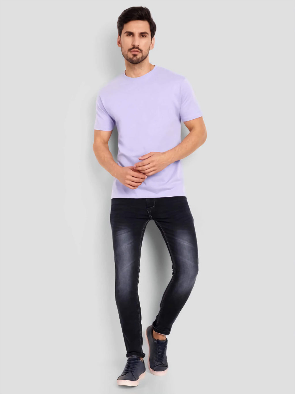 Man wearing a light purple t-shirt and black jeans on a gray background