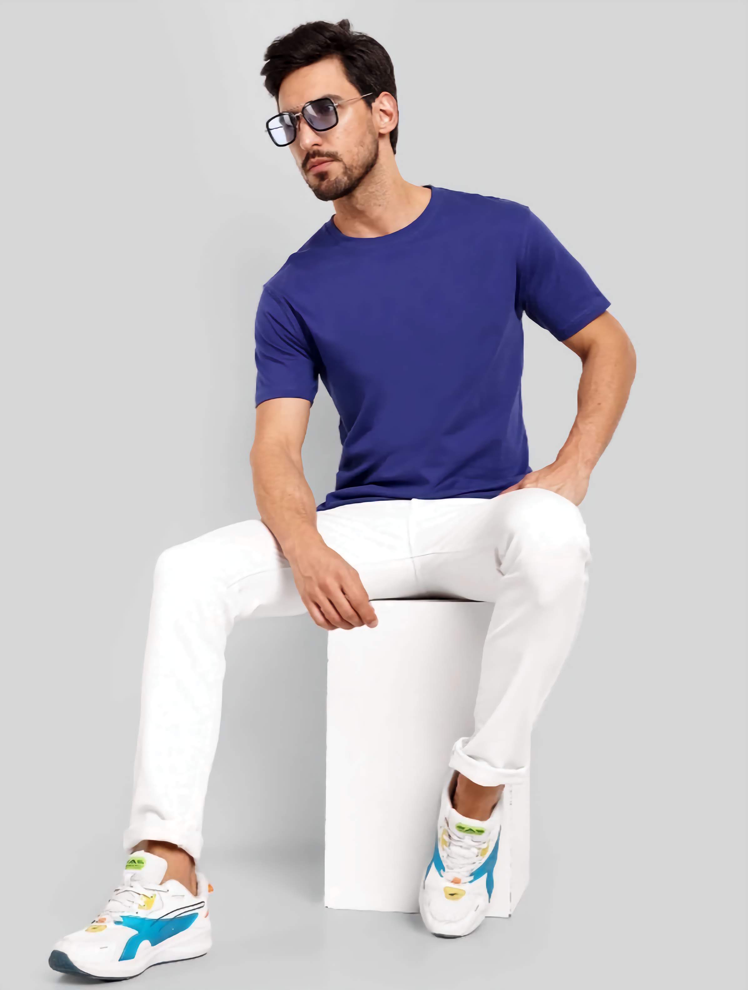 Man wearing a blue t-shirt, white pants, and colorful sneakers on a gray background