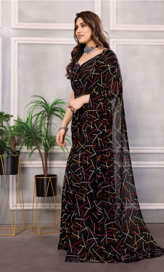 Woman wearing a black patterned dress standing in a room with plants and a gray wall.